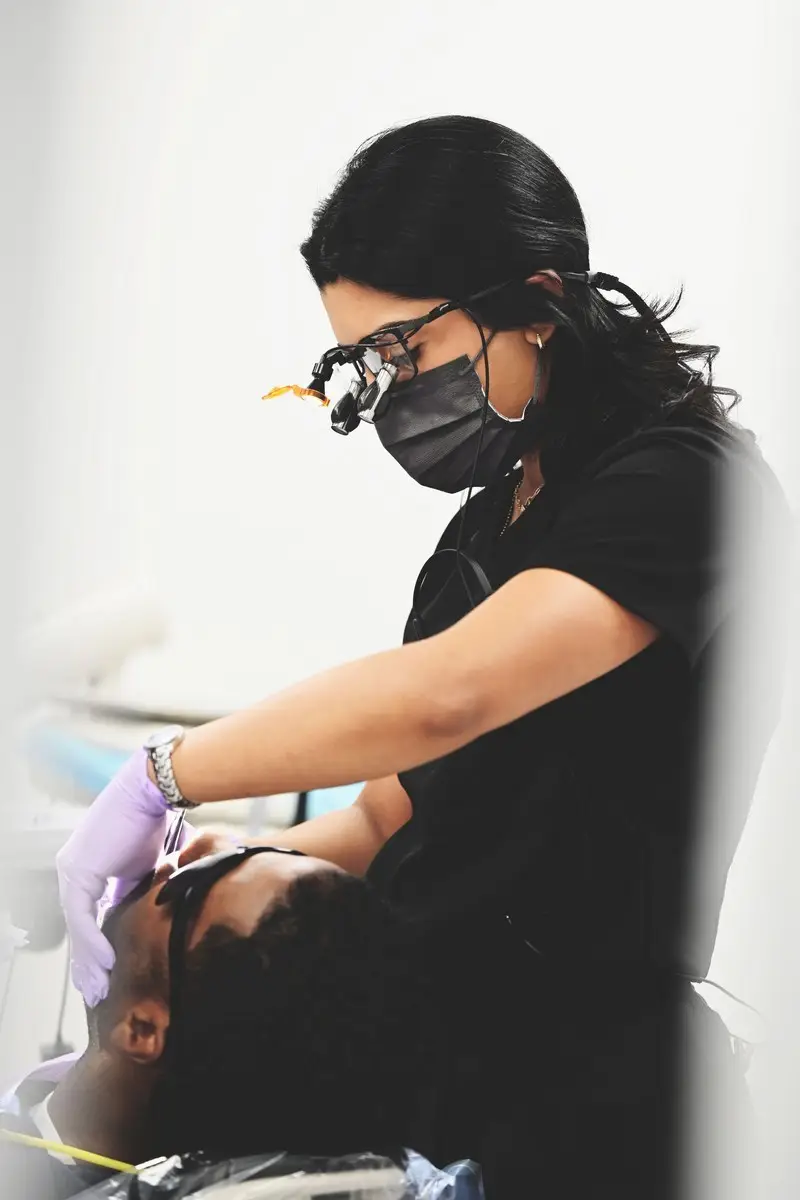 Dental professional using magnifying glasses to examine a patient's mouth during a dental procedure.