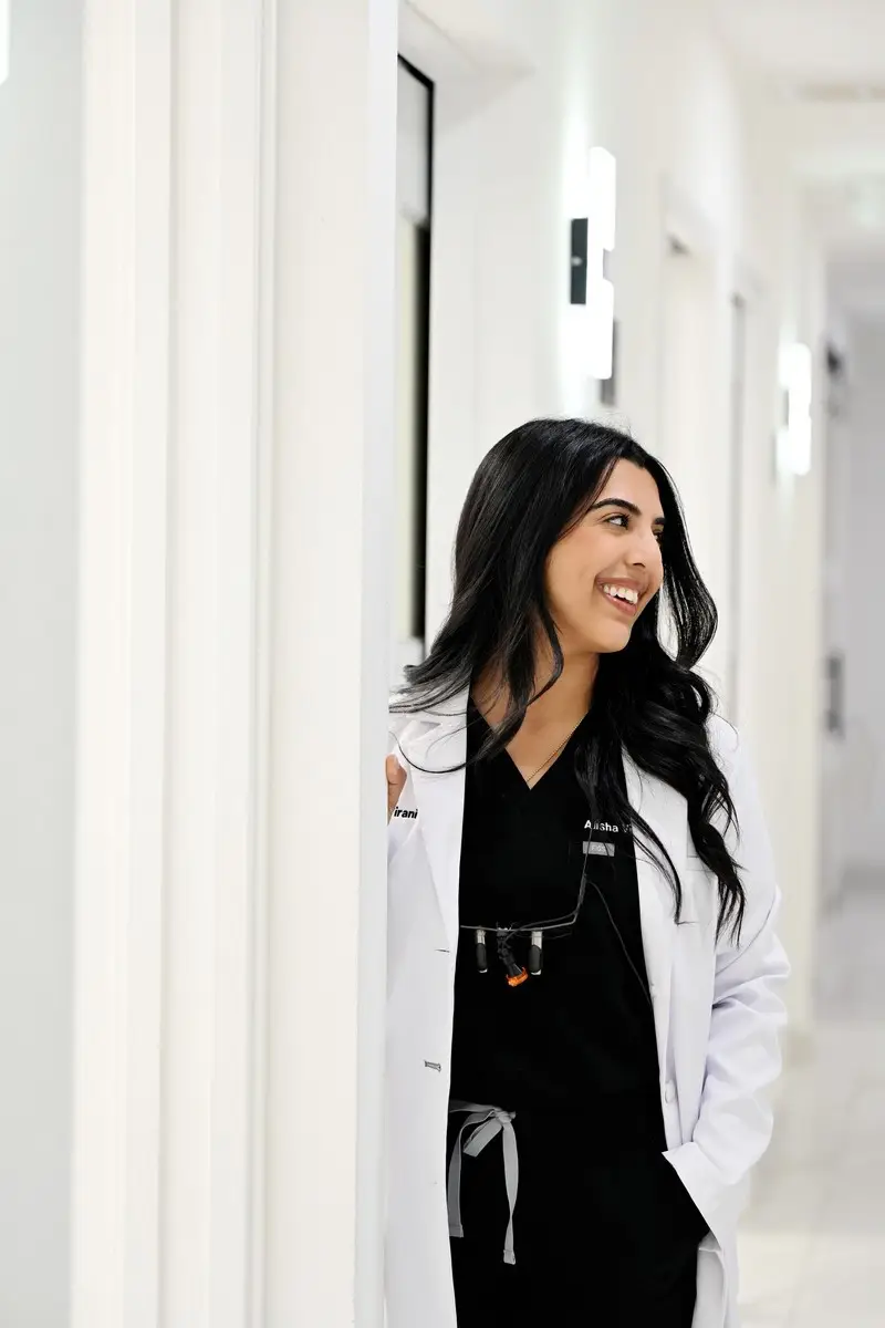 Smiling healthcare professional in a white lab coat standing in a modern clinic hallway.