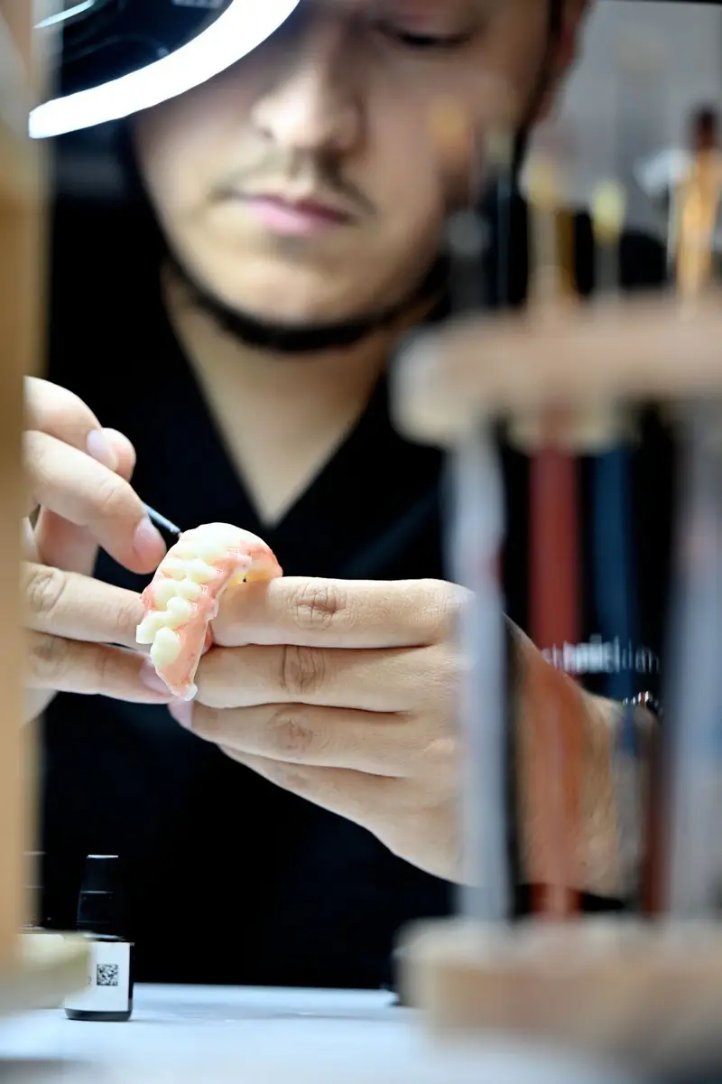 Dental technician crafting a dental model with precision tools in a lab setting.