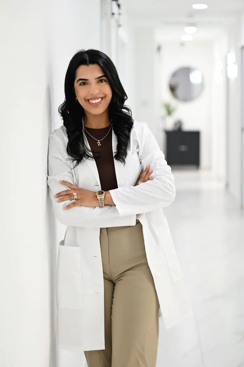 Smiling female doctor in a white lab coat standing in a modern clinic hallway.